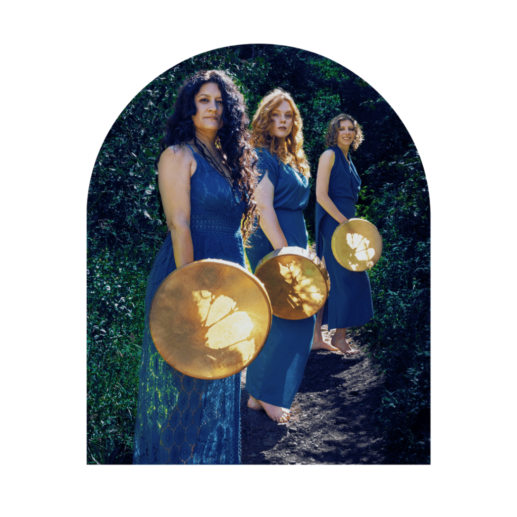 Three women holding shamanic drums standing in a healing forest